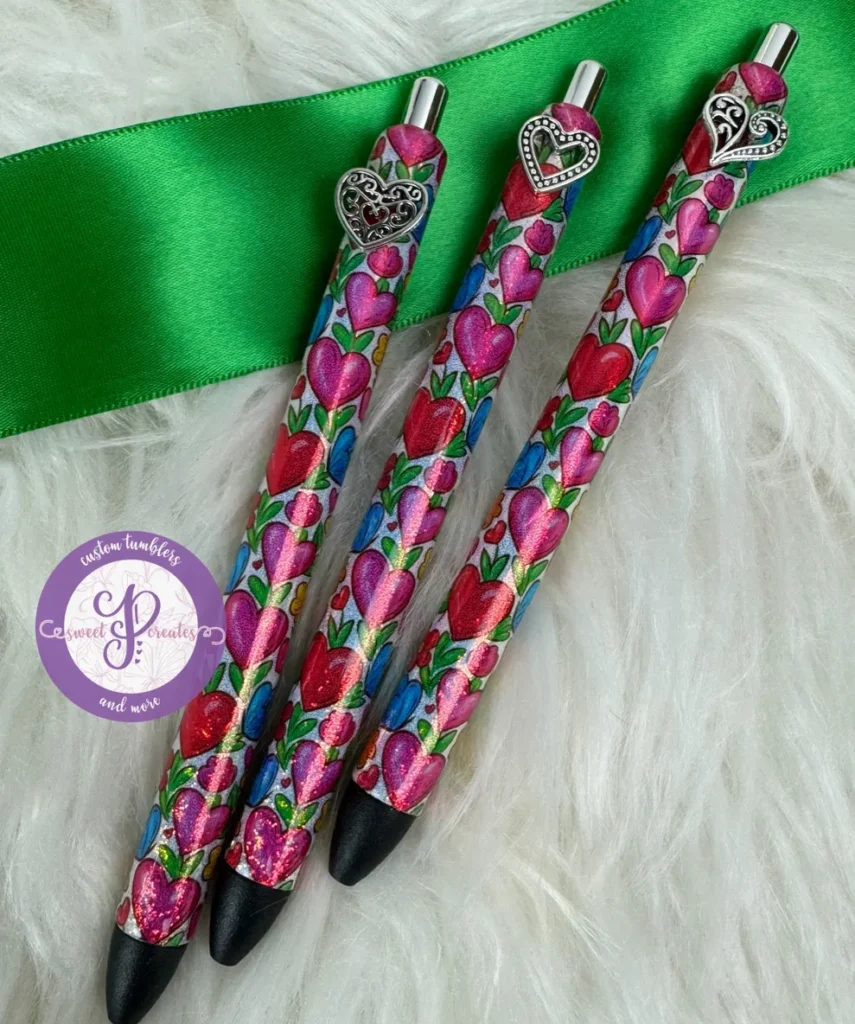 Colorful heart-covered pen trio beside ribbon