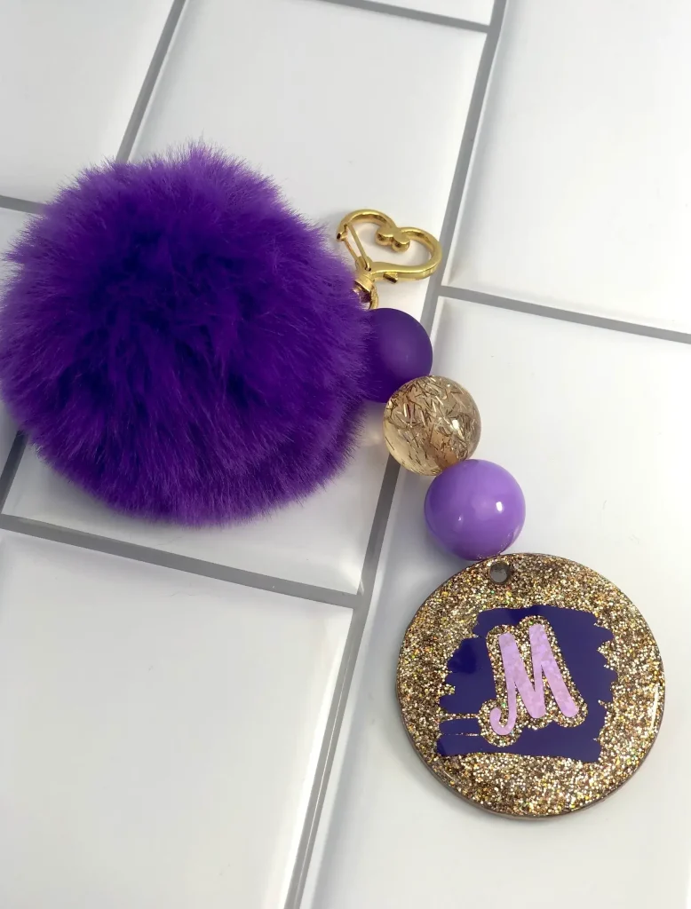 Purple pom pom keychain with decorative charm.